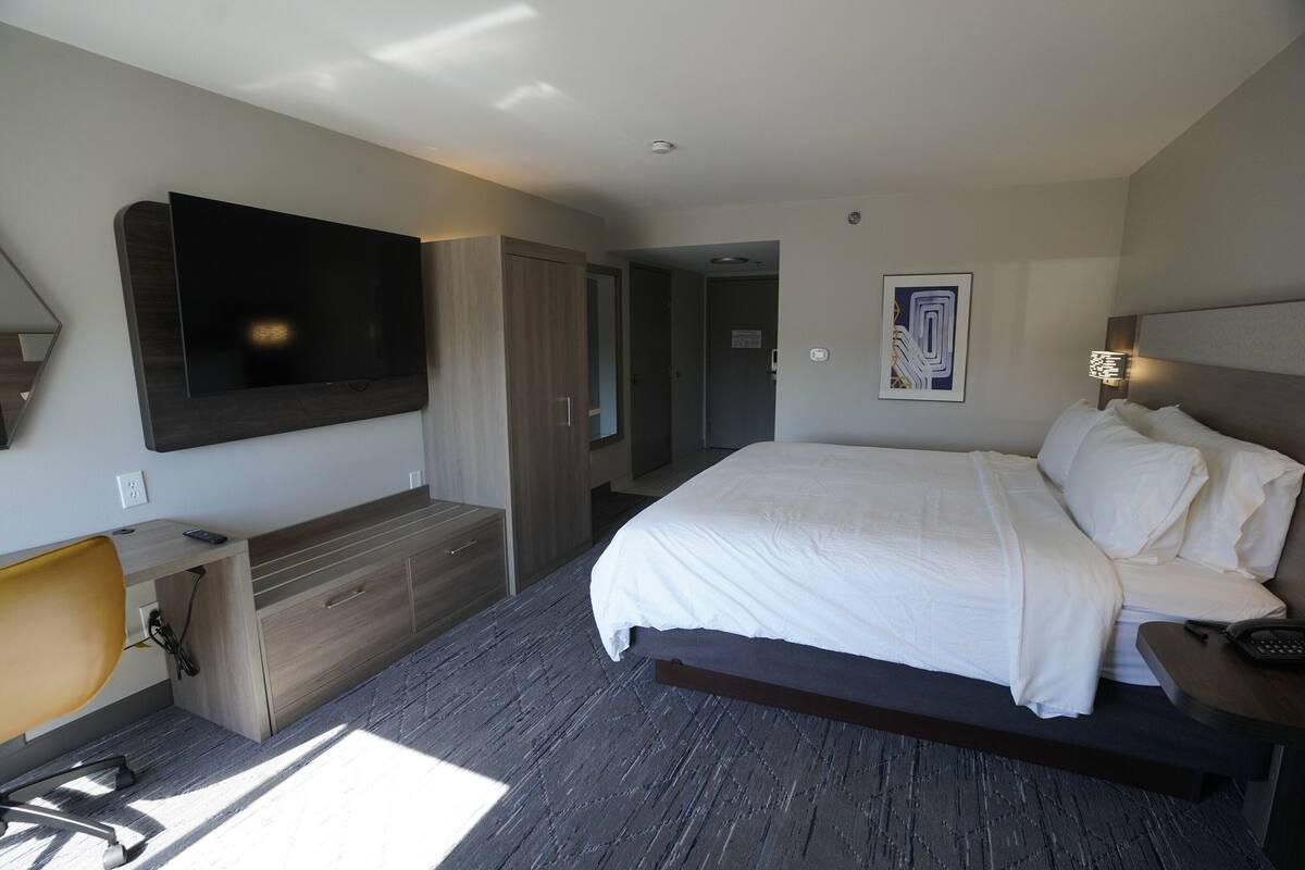 Een moderne hotelkamer met een groot bed, een flatscreen televisie aan de muur, een bureau met stoel, en een nachtkastje met lamp.