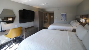 A hotel room with two beds, a desk, a chair, a TV, and a painting on the wall.