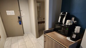 Un pasillo de hotel con una zona de kitchenette equipada con cafetera, microondas y alacenas.