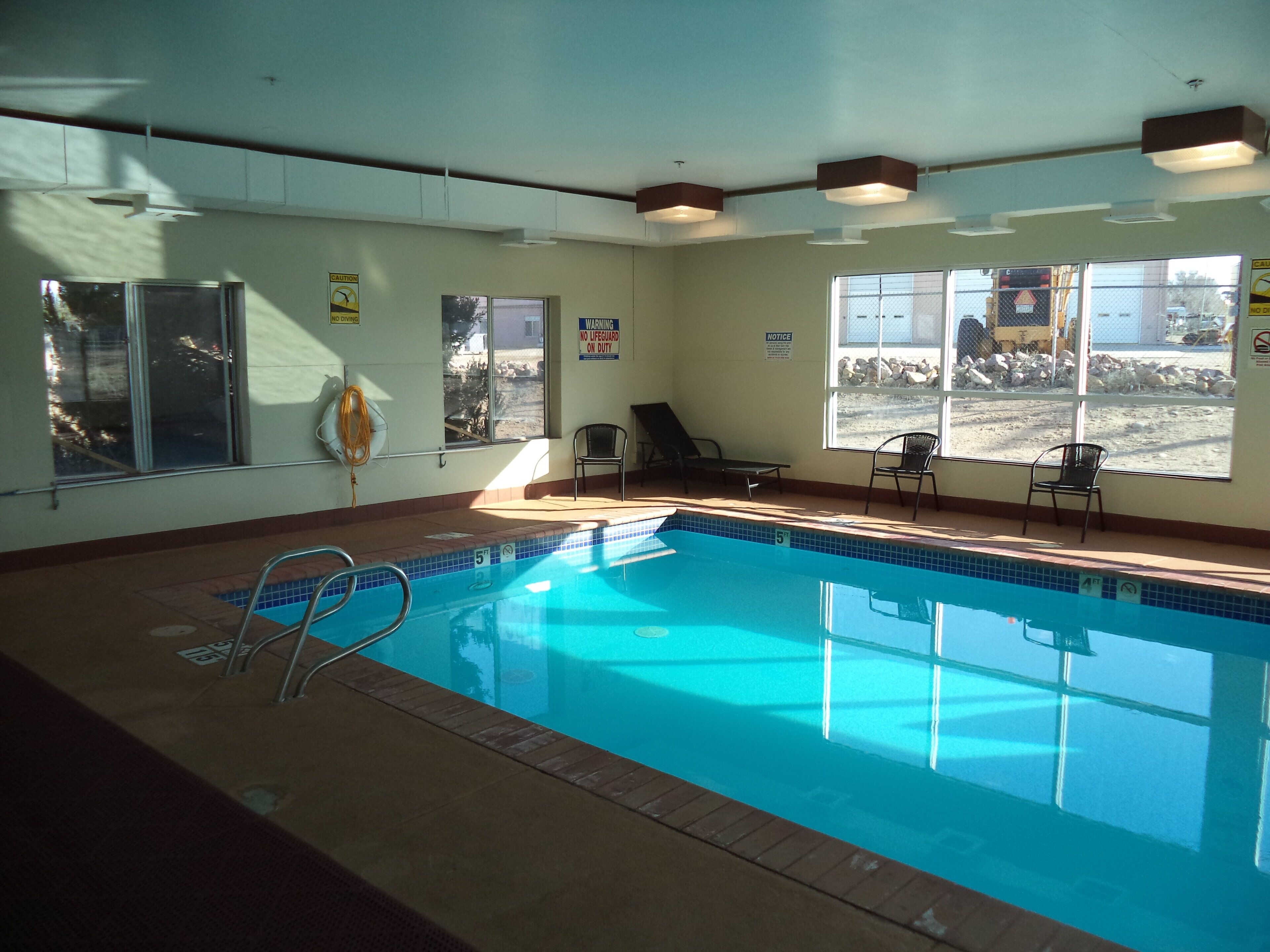 An indoor swimming pool with clear water, a lifeguard chair, and a view of a construction site through the windows.
