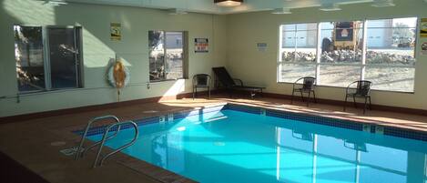 An indoor swimming pool with clear water, a lifeguard chair, and a view of a construction site through the windows.