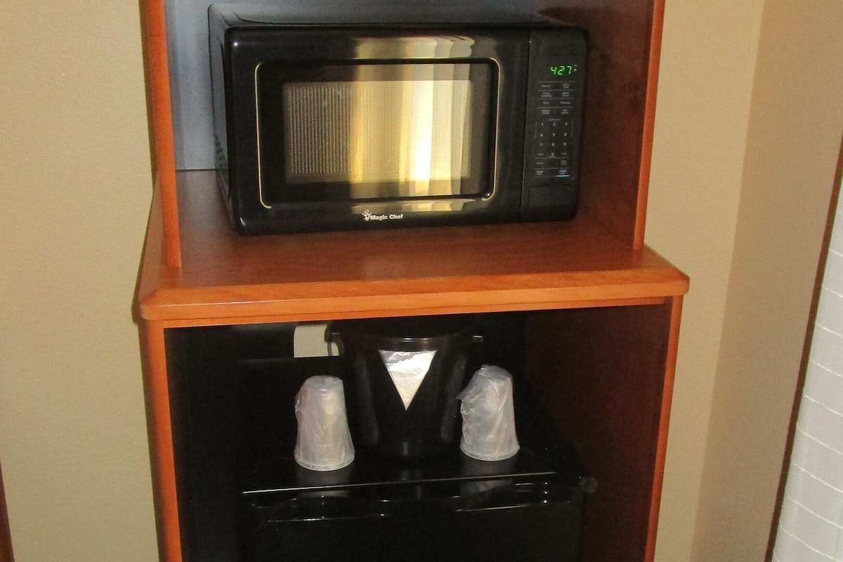 En minibar med mikrovågsugn, kaffebryggare och en flaska vatten.