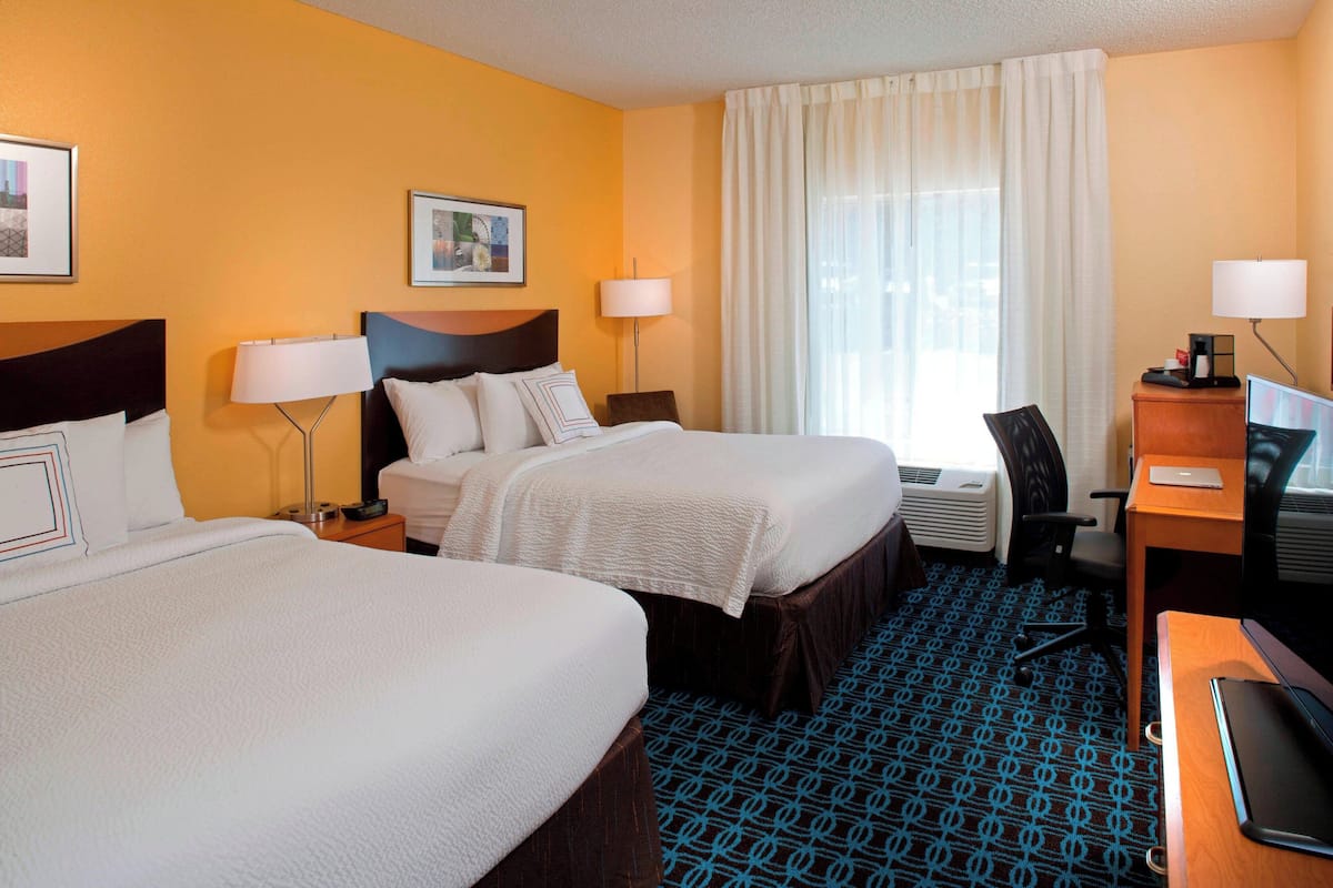 A hotel room with two beds, a desk, a chair, a television, and a window with curtains.