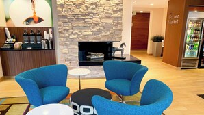 Eine moderne Lobby mit blauen Sesseln, einem kleinen runden Tisch, einer Steinwand, einem Kamin und einem Kiosk in der Ecke.