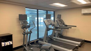 Ein Fitnessstudio mit Laufbändern, Crosstrainern und einem digitalen Bildschirm.