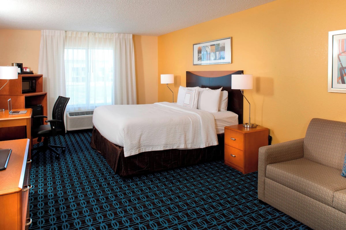 A hotel room with a bed, desk, chair, and a sofa.