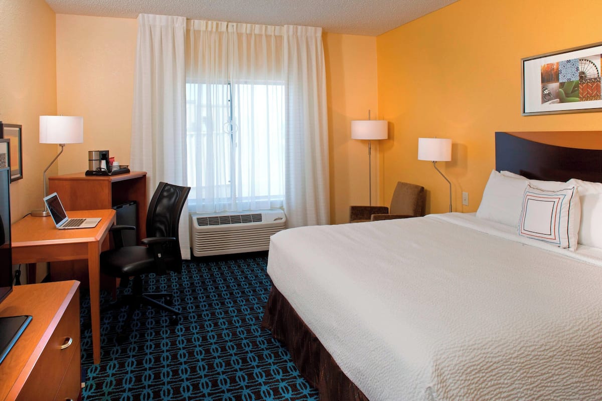 A hotel room with a bed, desk, chair, and air conditioning unit.