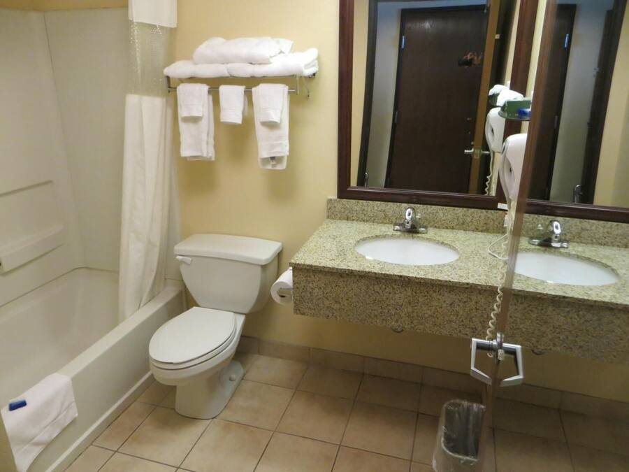 Un baño con inodoro, lavamanos y bañera. Hay toallas colgadas en un perchero sobre el inodoro.