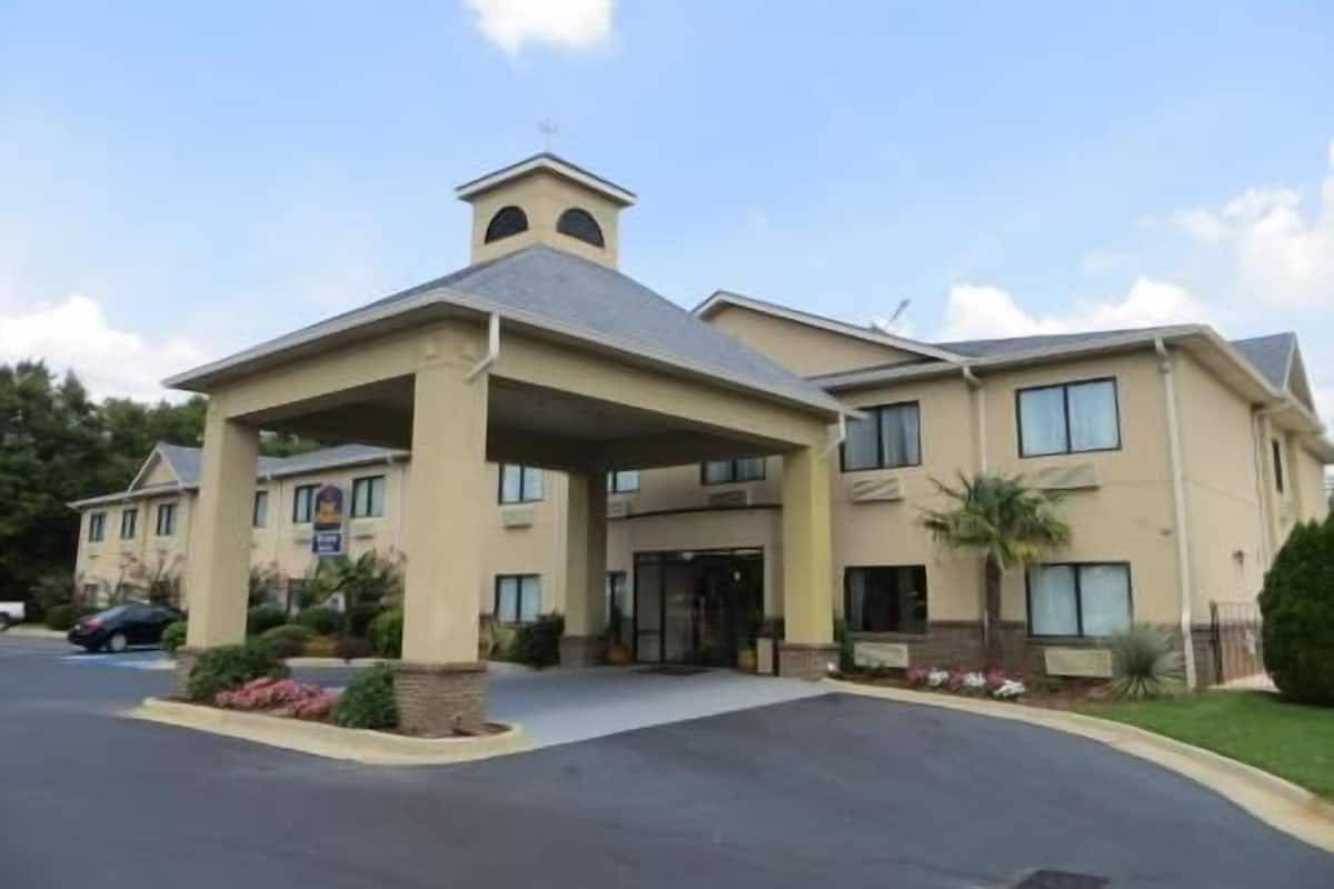 A multi-story hotel with a covered entrance, a bell tower, and a parking lot.
