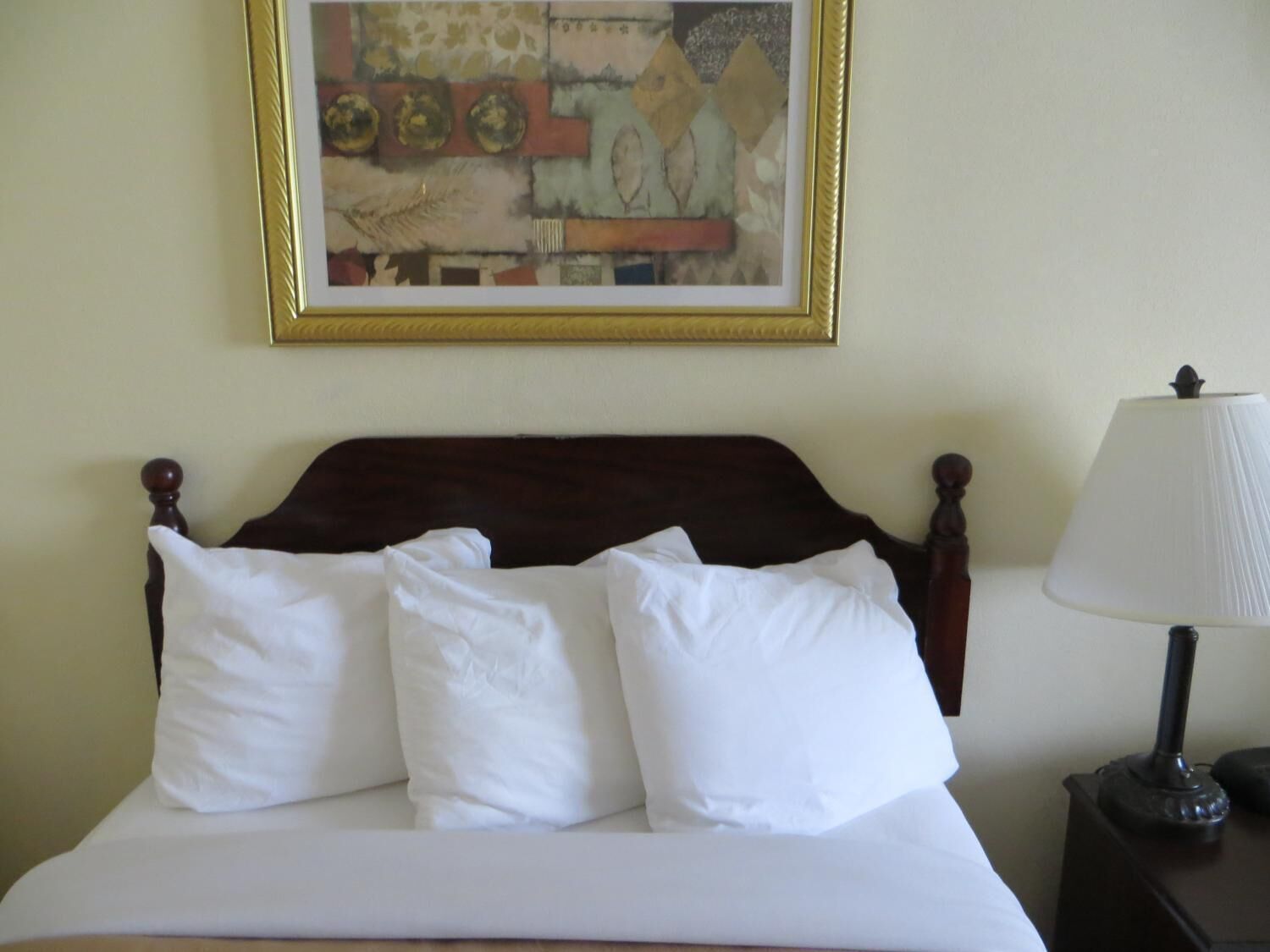 A bed with white bedding, a wooden headboard, and a framed abstract painting on the wall.