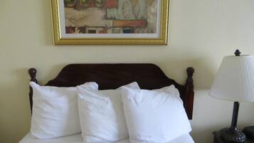 A bed with white bedding, a wooden headboard, and a framed abstract painting on the wall.