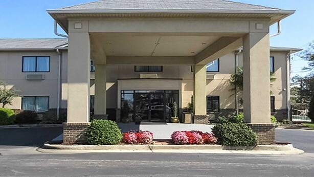 A building with a covered entrance, a small tower-like structure on the roof, and a parking lot in front.