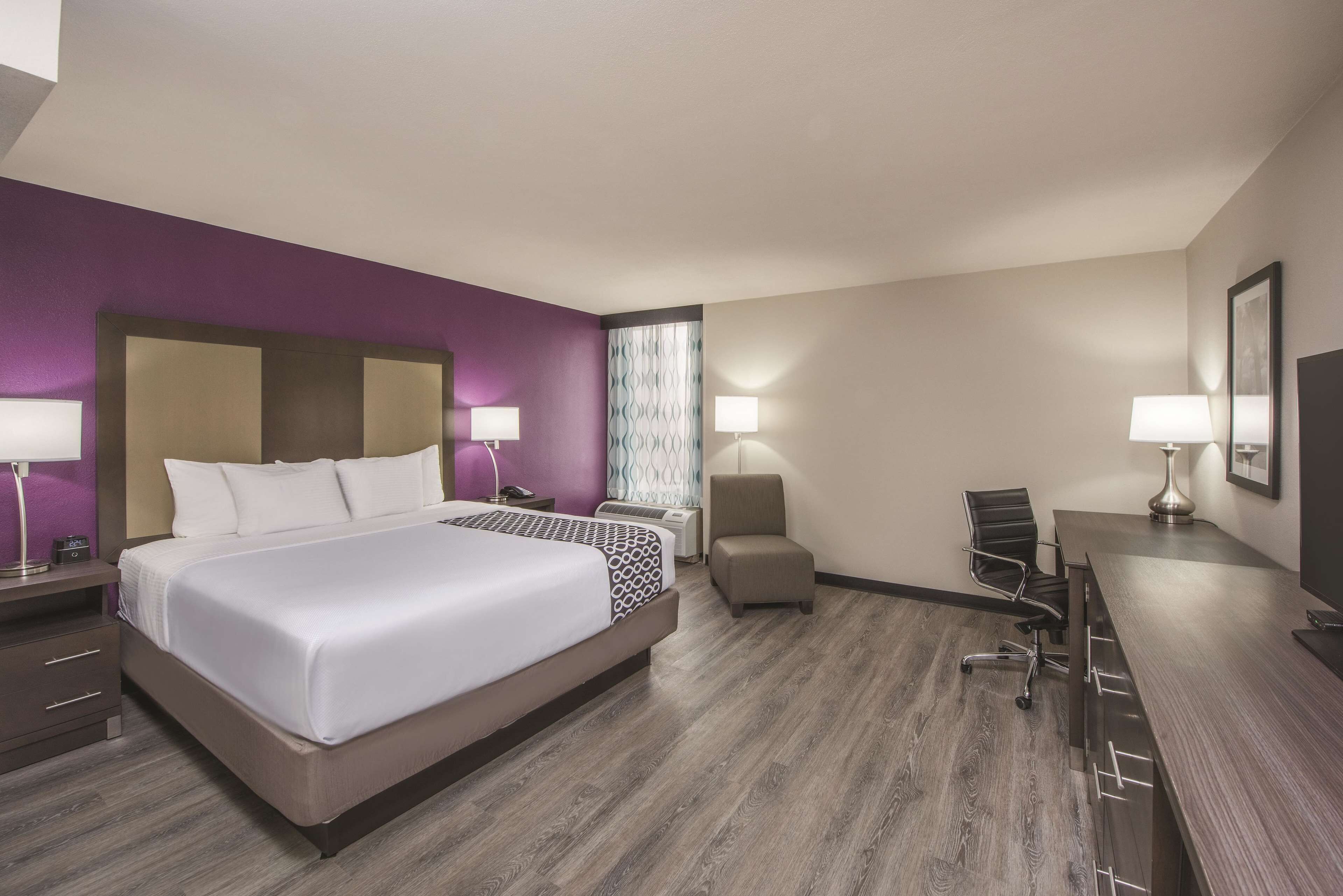 A hotel room with a large bed, a desk, a chair, and a small table.