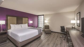 A hotel room with a large bed, a desk, a chair, and a small table.