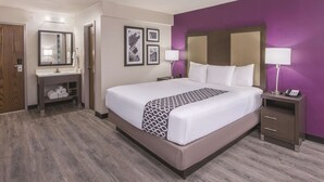 Een hotelkamer met een groot bed, een nachtkastje met een lamp, een kaptafel met spiegel en een muur met ingelijste foto's.