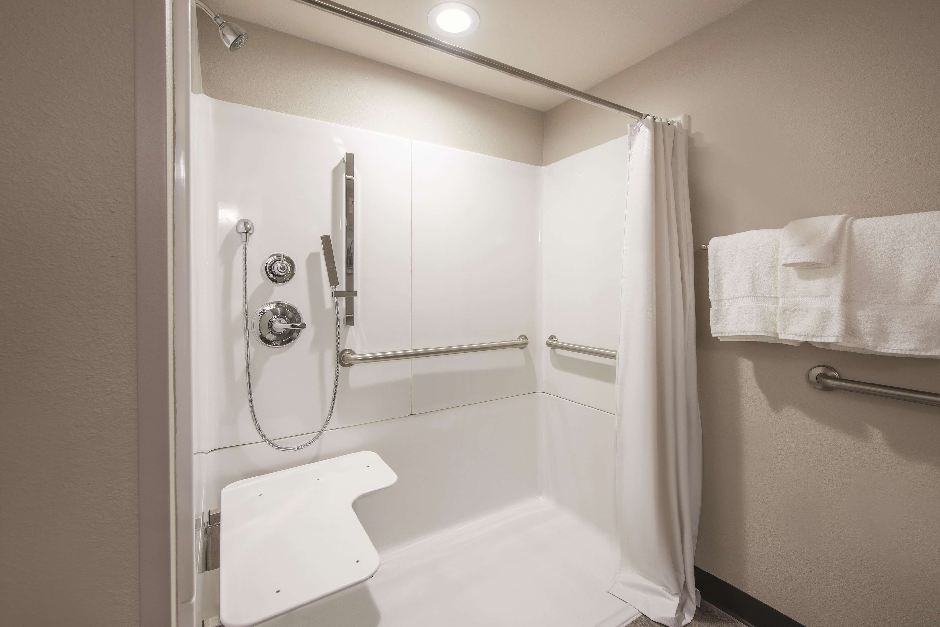 Un espace douche équipé de toilettes blanches, de barres d’appui et d’un rideau de douche.