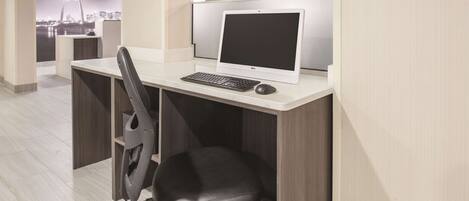 A modern office cubicle with a Dell desktop computer, a black office chair, and a view of a cityscape through a glass wall.
