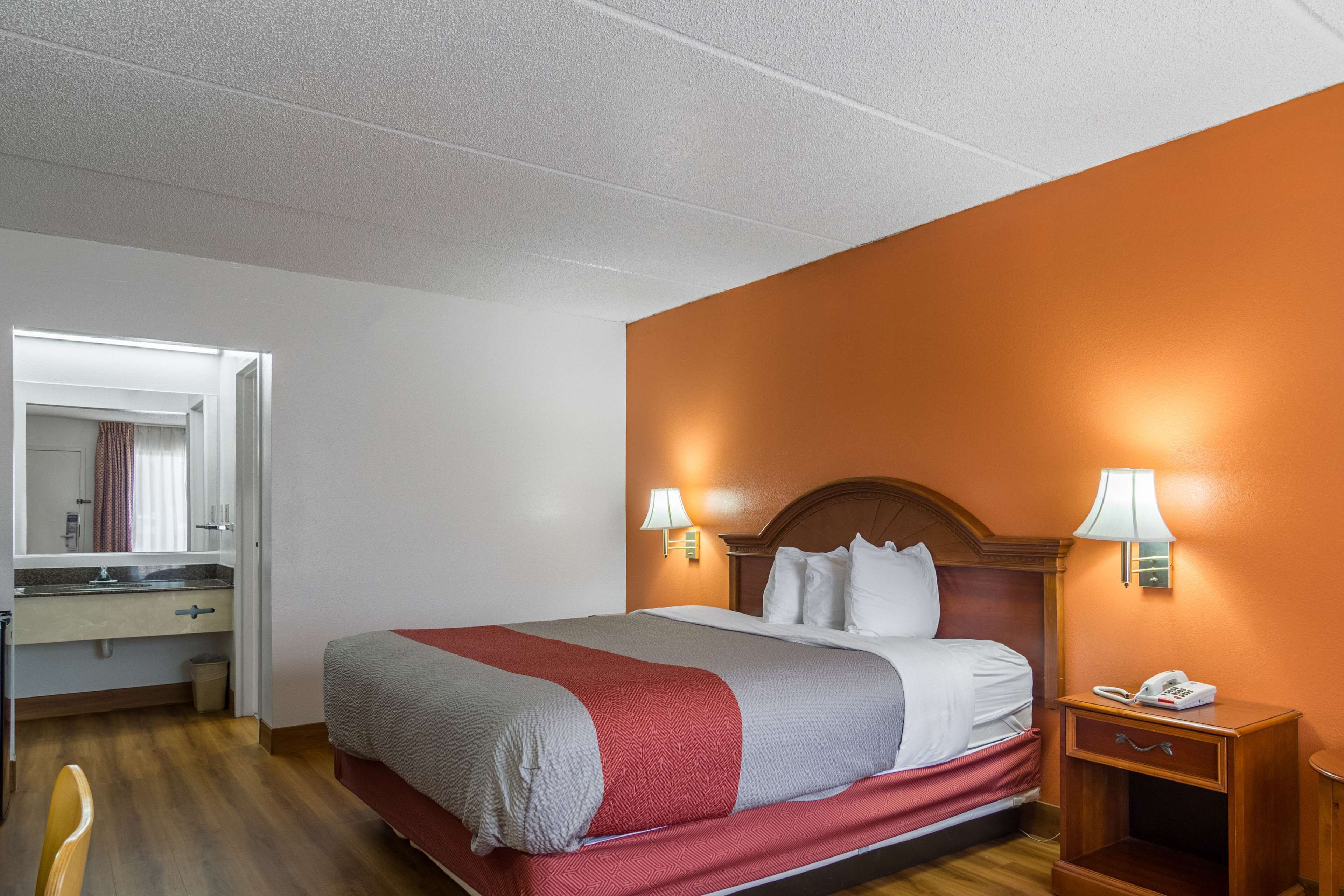 A hotel room with a bed, bedside lamps, a nightstand with a phone, a mirror, and a wooden floor.
