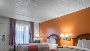 Una habitació d'hotel amb dos llits, una taula, una cadira, una làmpada i un telèfon.