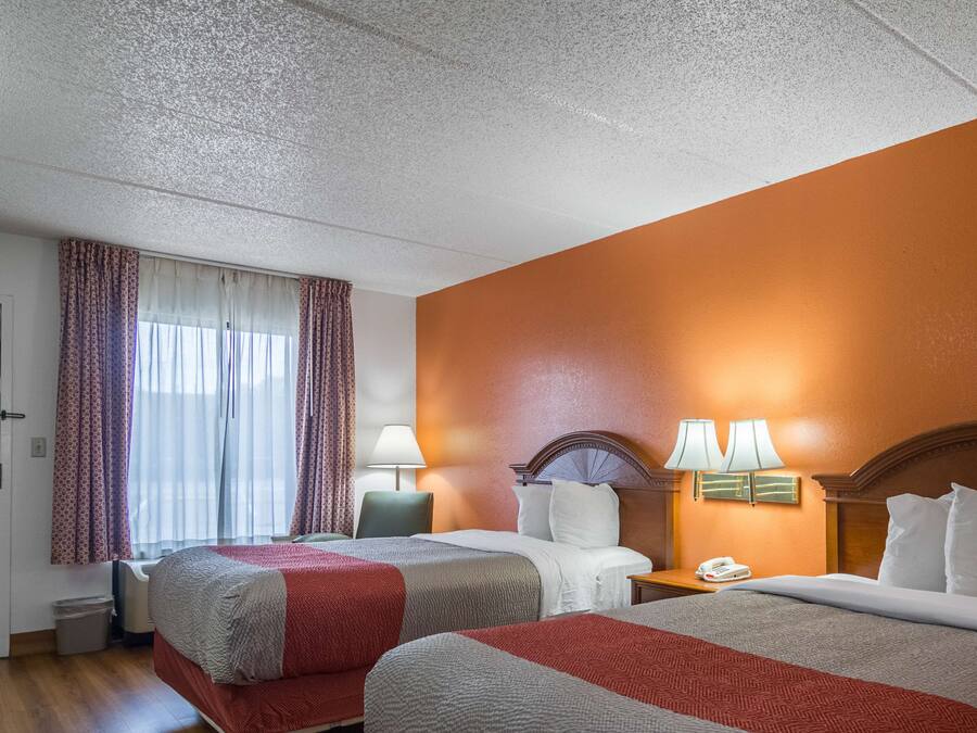 Una habitación de hotel con dos camas, un escritorio, una silla, una lámpara y un teléfono.