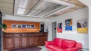 Una zona de recepció amb un taulell de fusta, un sofà de cuir vermell i una paret amb quadres i cartells emmarcats.