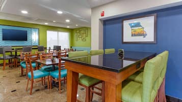A conference room with a large table, green chairs, a TV, and a framed picture on the wall.