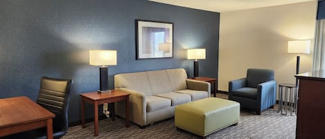 A hotel room with a sofa, armchair, ottoman, desk, and lamps.