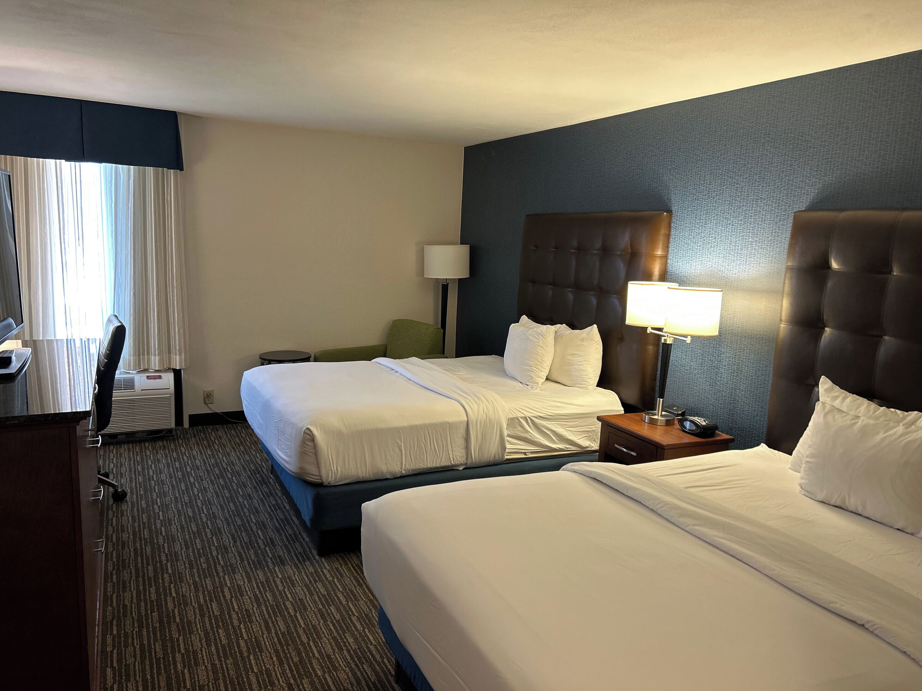Une chambre d’hôtel avec deux lits, un bureau, une chaise, une lampe et une table de chevet.