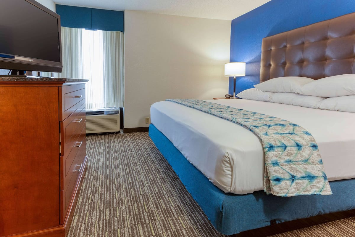 A hotel room with a bed, a dresser, a television, and a window with curtains.