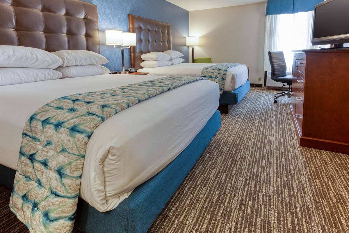 A hotel room with two beds, a large headboard, a desk with a chair, and a television.