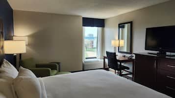A hotel room with a bed, a desk, a chair, a TV, and a window with a view of buildings.