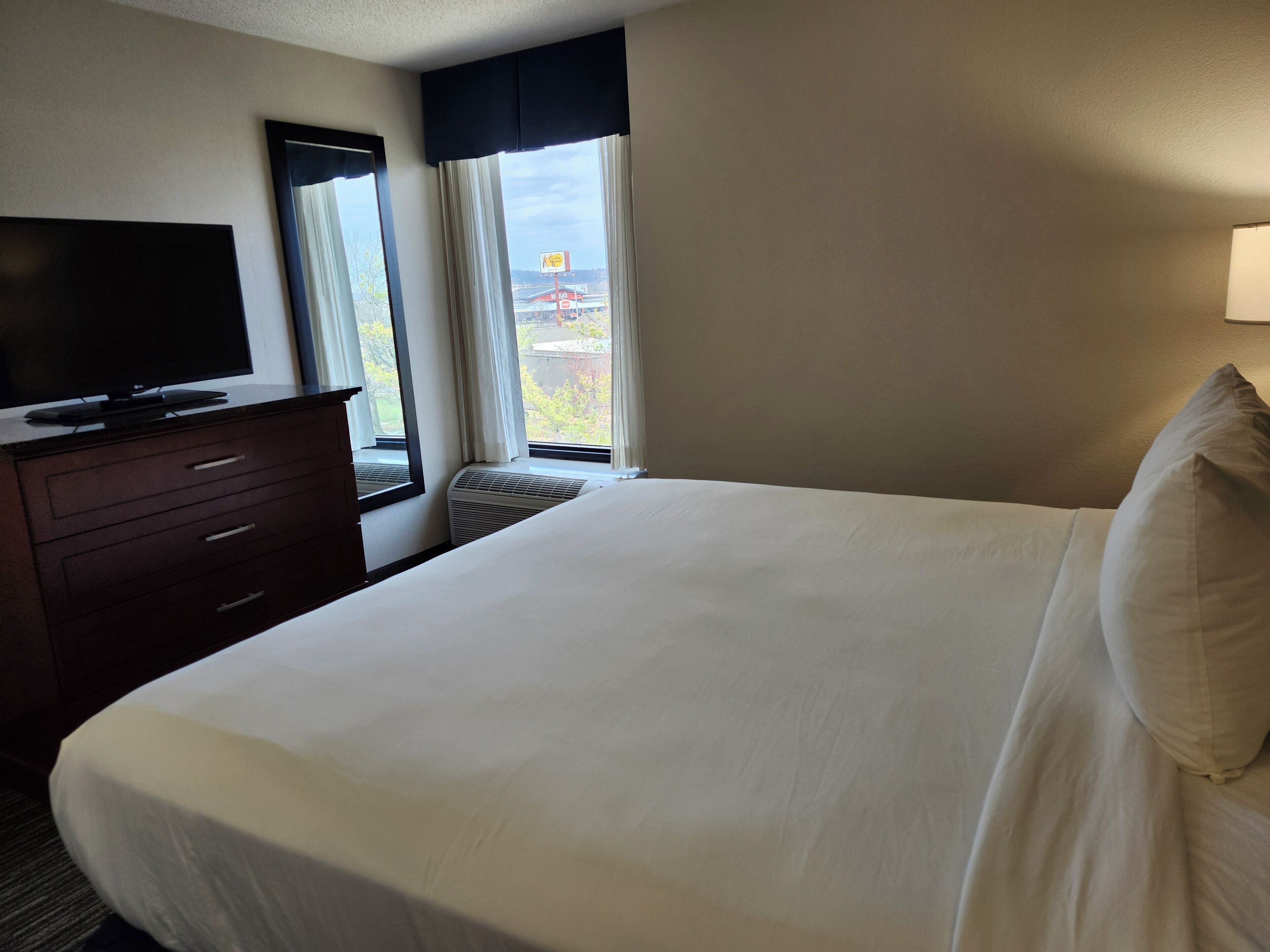 A hotel room with a bed, a TV on a dresser, and a window with curtains.