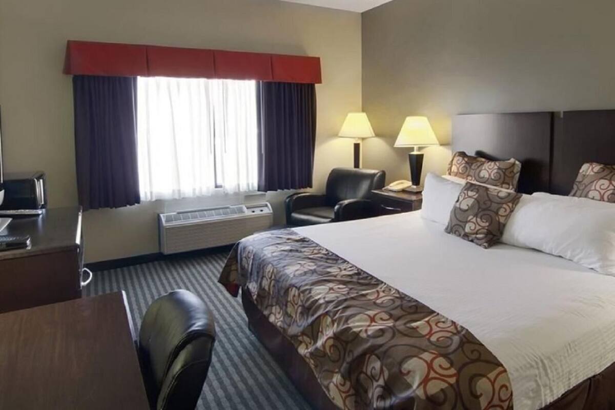 A hotel room with a large bed, two bedside lamps, a desk with a chair, and a window with curtains.