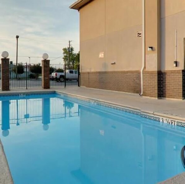 A swimming pool with a clear blue water surface, surrounded by a low brick wall and a metal fence. - Econo Lodge (Waynesboro)