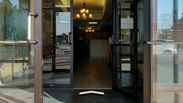 Entrada de un hotel con puerta de cristal, se aprecia el interior con un candelabro y un cartel que indica la zona de estacionamiento.