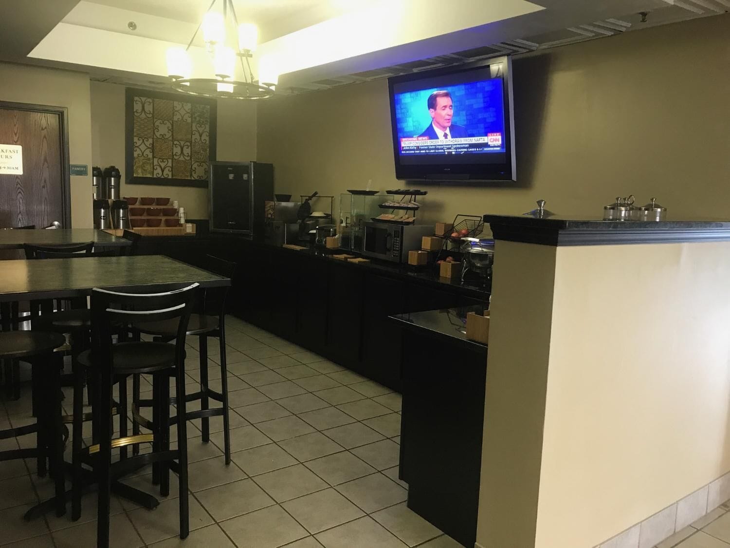 Een keuken met een televisie waarop een nieuwskanaal wordt vertoond, een koffieapparaat en een koelkast.