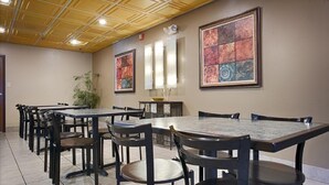 Un salón de conferencias con varias mesas y sillas, un techo con diseño de cuadrícula y obras de arte en las paredes.