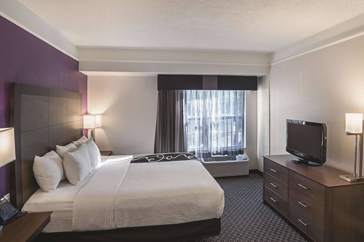 Une chambre d’hôtel avec un grand lit, un téléviseur à écran plat, un bureau avec un téléphone et une fenêtre avec des rideaux.