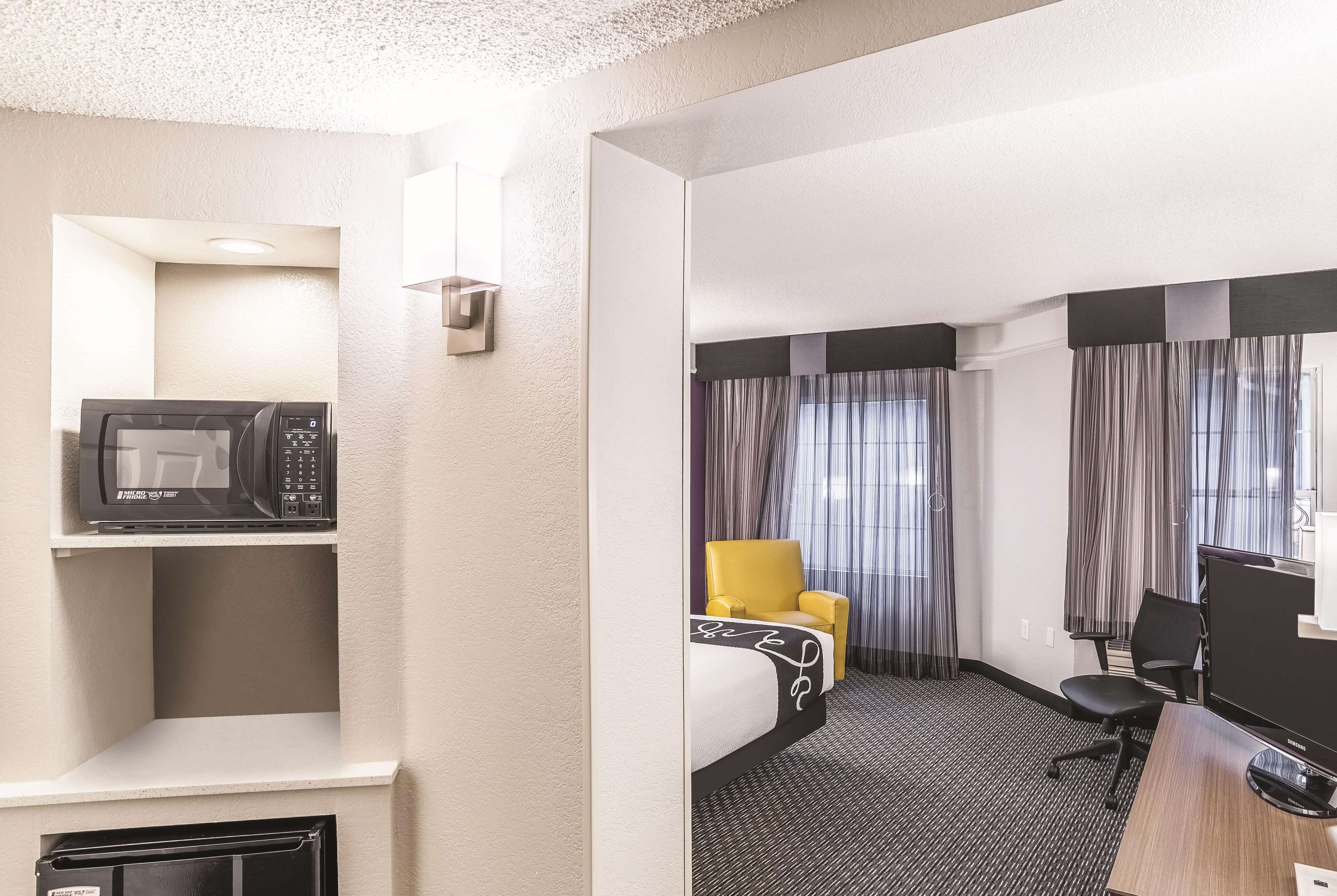 A hotel room with a bed, a desk, a chair, a microwave, and a television.