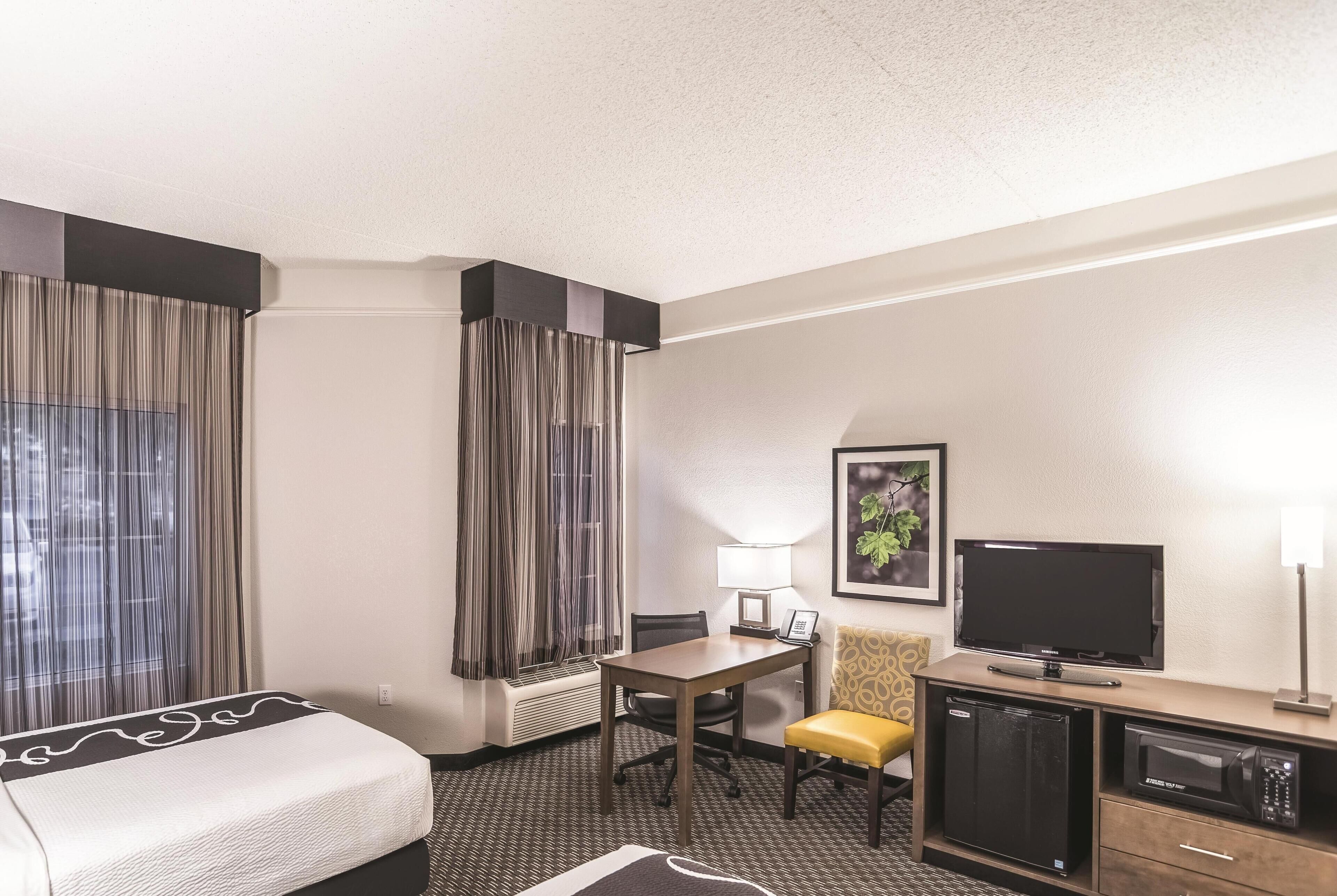 Hotelkamer met een bed, bureau, stoel, televisie, magnetron en kleine koelkast.