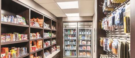 Un rayon de supermarché avec des étagères remplies d’en-cas et de boissons, un présentoir réfrigéré et un mur où sont suspendus des produits emballés.