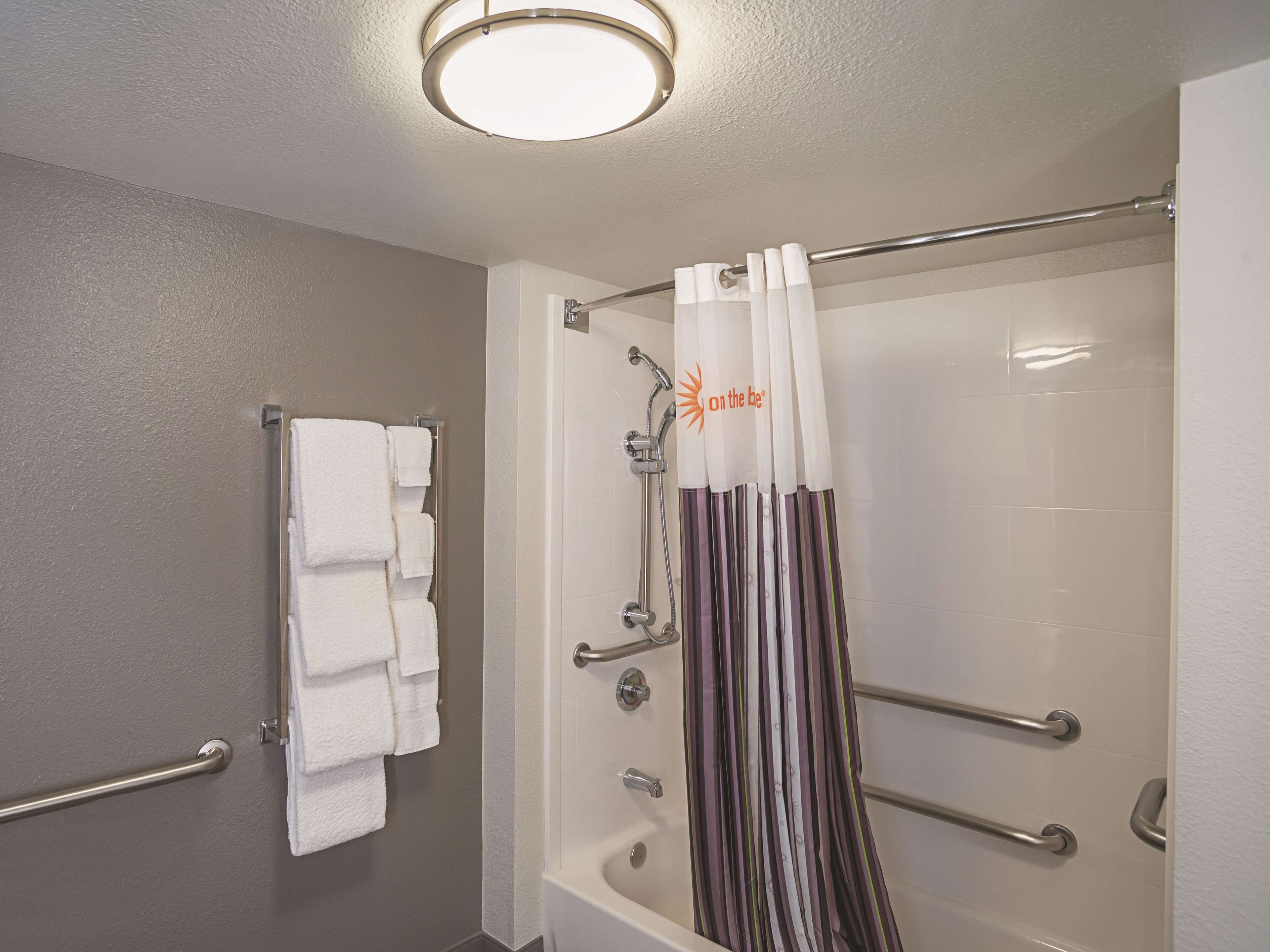 A bathroom with a shower, a towel rack with multiple towels, and a shower curtain with a sun design.