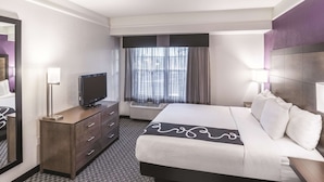 A hotel room with a bed, a TV, a dresser, a mirror, and a window with curtains.