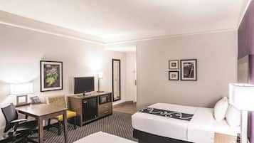 A hotel room with a bed, desk, chair, television, and two framed pictures on the wall.