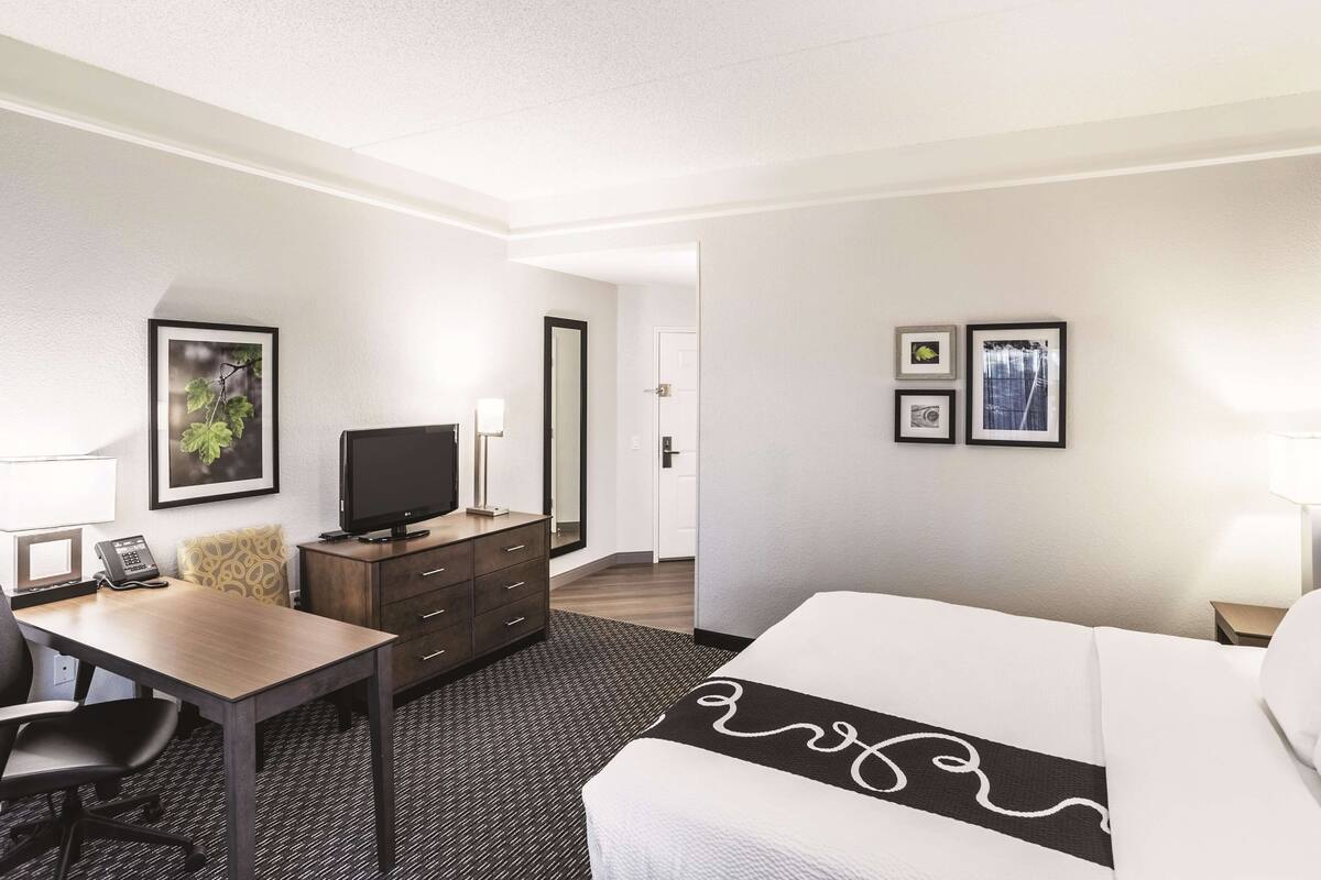 Une chambre d’hôtel comprenant un lit, un bureau avec une chaise, une télévision, une commode et une porte.