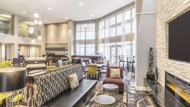 A spacious lobby with a high ceiling, large windows, a fireplace, and a variety of seating arrangements.