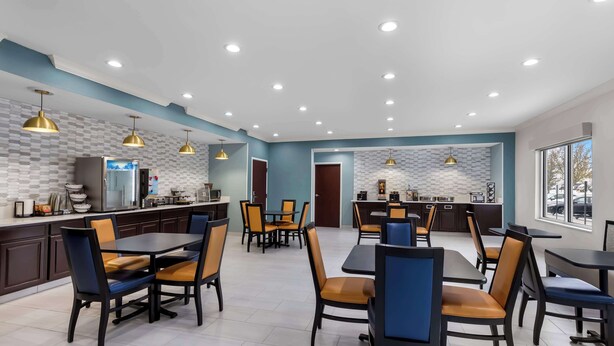 Un comedor moderno con varias mesas y sillas, luces empotradas en el techo y una cocina al fondo.