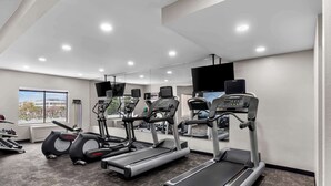 Un gimnasio con cintas de correr, máquinas elípticas y un espejo grande.