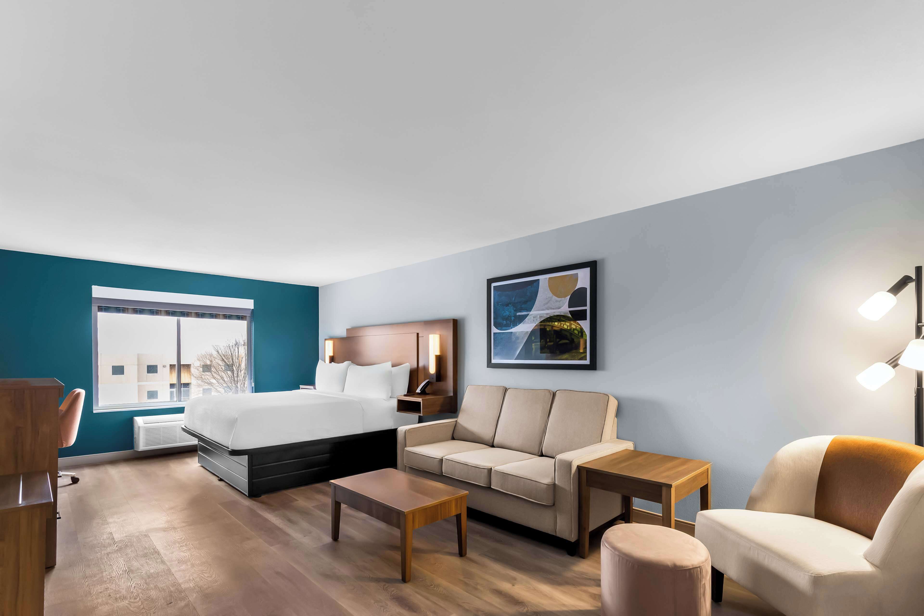 A modern hotel room with a bed, sofa, coffee table, and a desk.