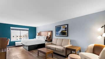 A modern hotel room with a bed, sofa, coffee table, and a desk.
